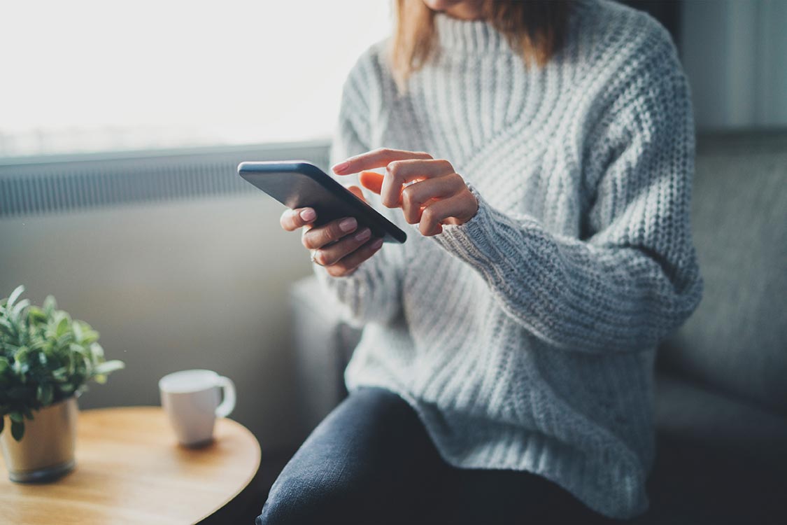 woman sitting on couch shopping on smartphone